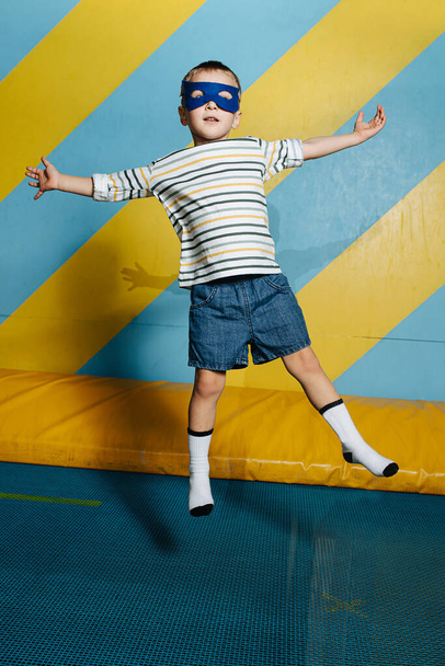 Awkward funny cute boy in mask jumping on trampoline in entertainment center in - Fotoğraf, Görsel