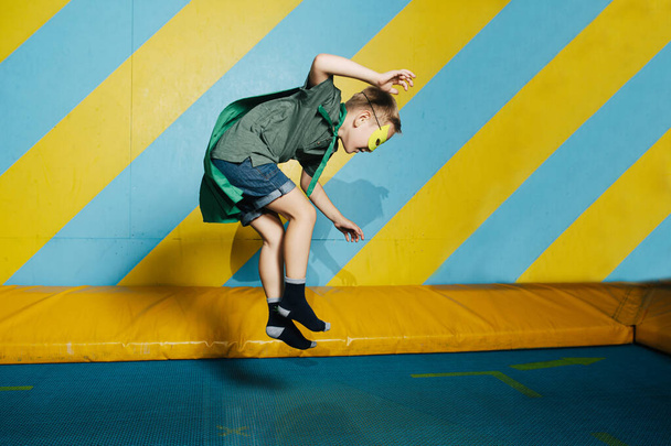 Garçon en masque et cape sautant sur trampoline dans le centre de divertissement - Photo, image