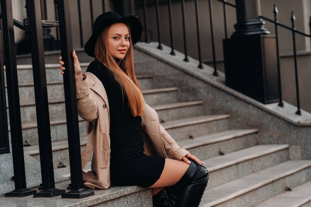 Stylish young woman in a beige coat in a black hat on a city street. Women's street fashion. Autumn clothing.Urban style. - Foto, Imagem