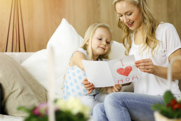 Happy mother day in sunny flat. Child daughter congratulates mom and gives her postcard with heart drawing. Family concept - Valokuva, kuva