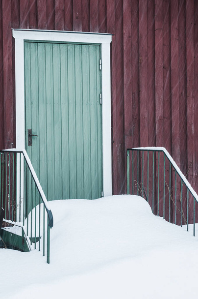 El edificio rojo cubierto de nieve con una puerta verde - Foto, Imagen