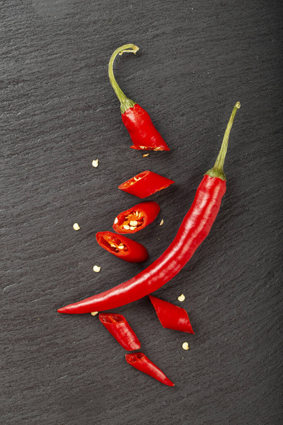 Red whole and chopped chile peppers on a black slate board. Spicy food concept. Space for text. Top view. - Фото, зображення