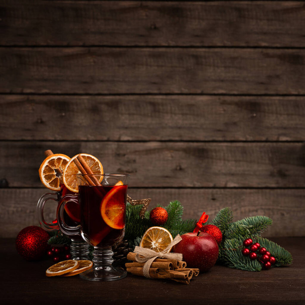 Mulled wine with cinnamon sticks orange fir tree branch and baubles Christmas composition over dark wooden background - Foto, Imagem
