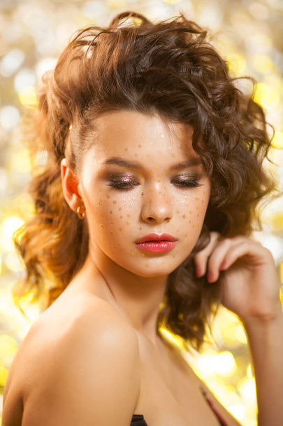 Creative winter makeup with golden snowflakes on her face and wavy hairstyle - Photo, image
