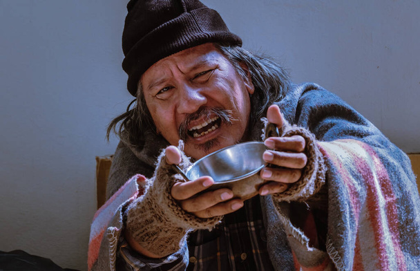 Ένα κοντινό πορτραίτο ενός άστεγου καθώς απλώνει μια κούπα και ζητάει βοήθεια. Μένει στο πεζοδρόμιο λόγω των 19 πανδημιών.. - Φωτογραφία, εικόνα