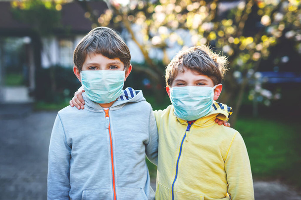 Two kids boys in medical mask as protection against pandemic coronavirus disease. Children, lovely siblings and best friends using protective equipment as fight against covid 19. - Photo, Image