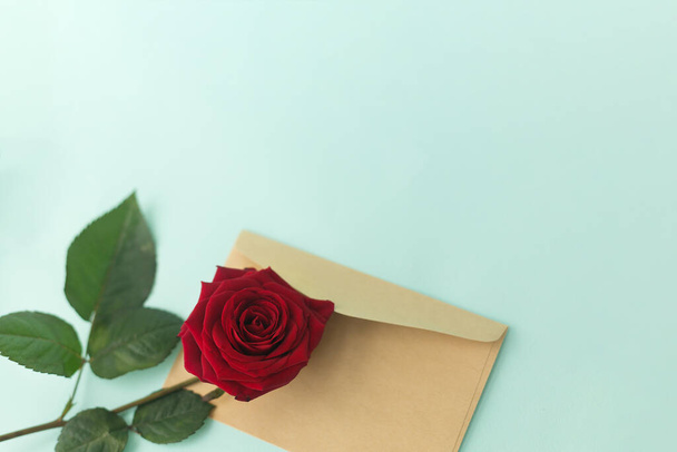 Red rose and envelope on a light green background. Minimalist concept for your mockup and project. Layout, flat lay, copy space, top view. Selective focus. - Фото, изображение