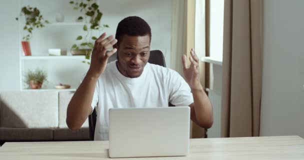 Mutlu şevkli afro-amerikalı adam beyaz günlük tişört giyiyor masaya oturuyor dizüstü bilgisayar ekranına bakıyor olumlu sınav sonuçları okuyor iyi haberler öğreniyor büyük ikramiye, başarı konsepti - Video, Çekim