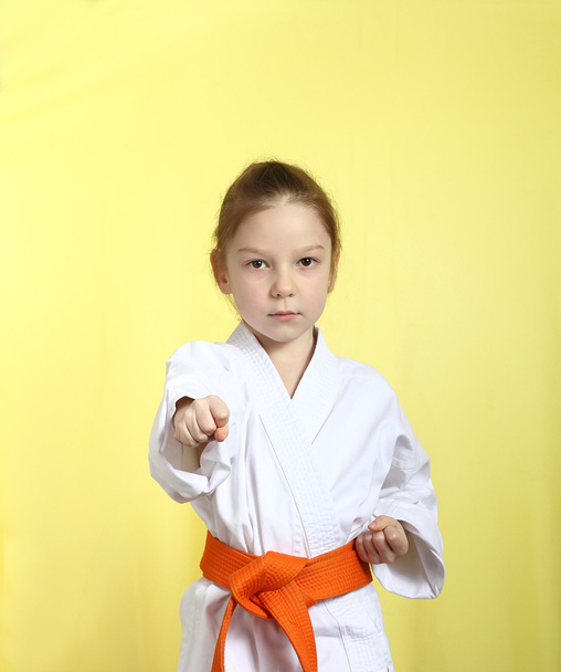 Girl on a yellow background with orange belt is hitting right hand - Φωτογραφία, εικόνα