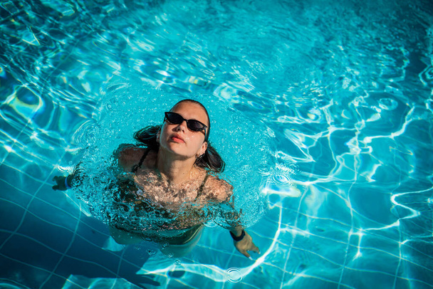Modeporträt eines anmutigen netten Mädchens mit stylischer Sonnenbrille, das während des Urlaubs im Luxus-Resort im Pool posiert. Fröhlich plus Größe Teenager Mädchen genießen. glücklich, positive Emotion, sommerlicher Stil. - Foto, Bild