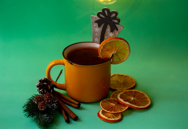 taza amarilla con té de Navidad con canela y naranja seca sobre un fondo turquesa - Foto, Imagen