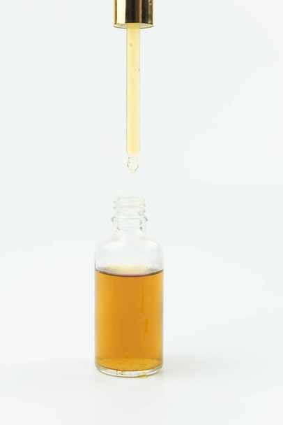 El aceite esencial cae desde la pipeta hasta el frasco aislado en blanco. Suero de esencia de aceite orgánico natural para la cara o el cuerpo en cuentagotas.  - Foto, Imagen