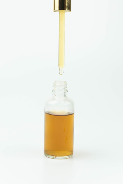 El aceite esencial cae desde la pipeta hasta el frasco aislado en blanco. Suero de esencia de aceite orgánico natural para la cara o el cuerpo en cuentagotas.  - Foto, Imagen