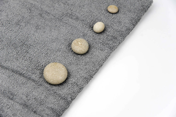 Graue Zen-Kieselsteine mit Handtuch auf Massagetisch im Schönheitssalon. Massage mit heißen Steinen. Konzeptset aus Harmonie, Balance und Meditation, Wellness, Entspannung, Wellness-Behandlung - Foto, Bild