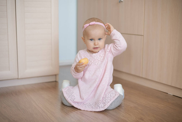 A one-year-old baby in a cute pink dress with a tulle skirt sits on the floor - Φωτογραφία, εικόνα