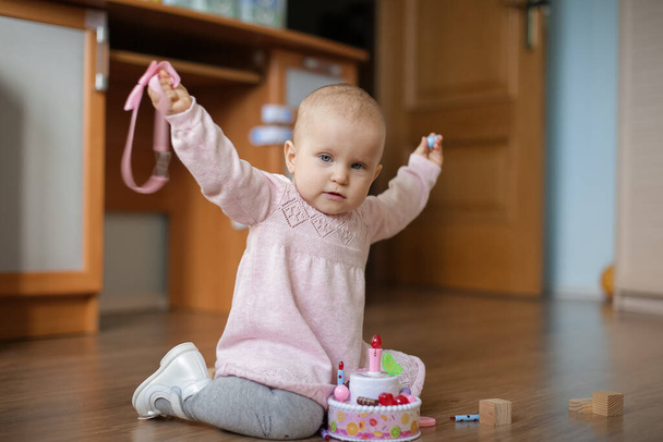 A one-year-old baby in a cute pink dress with a tulle skirt sits on the floor - Valokuva, kuva