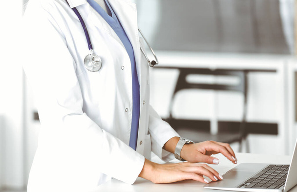 Unknown female physician using laptop computer, close-up. Woman-doctor at work in clinic. Medicine concept - 写真・画像