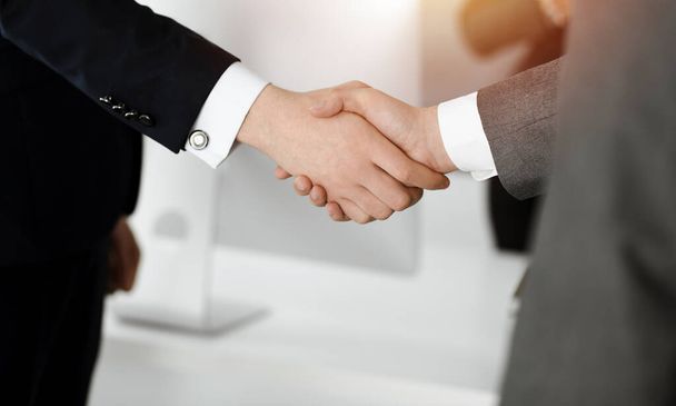 Unknown businessman shaking hands with his colleague or partner while standing straight in sunny office, close-up - Φωτογραφία, εικόνα