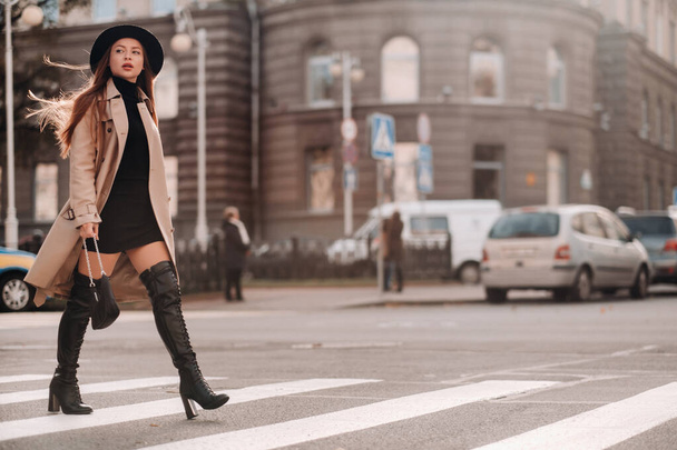 都会の通りの黒い帽子のベージュのコートを着たスタイリッシュな若い女性。女性のストリートファッション。秋服｜Urban Style. - 写真・画像