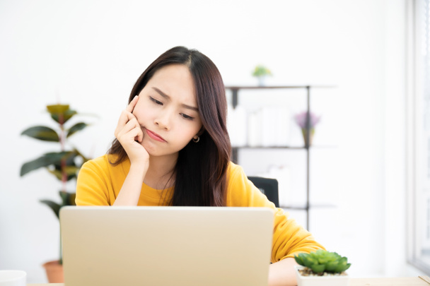 Азійська молода жінка серйозно працює вдома над комп'ютерним ноутбуком. Вона думає знайти вирішення проблеми роботи. - Фото, зображення