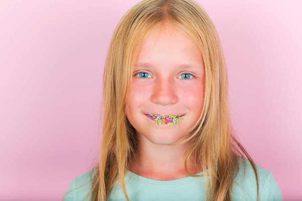 Menina desfrutando em doces doces. Menina com polvilhas de açúcar multicoloridas em seus lábios. Dependência de açúcar em crianças - Foto, Imagem