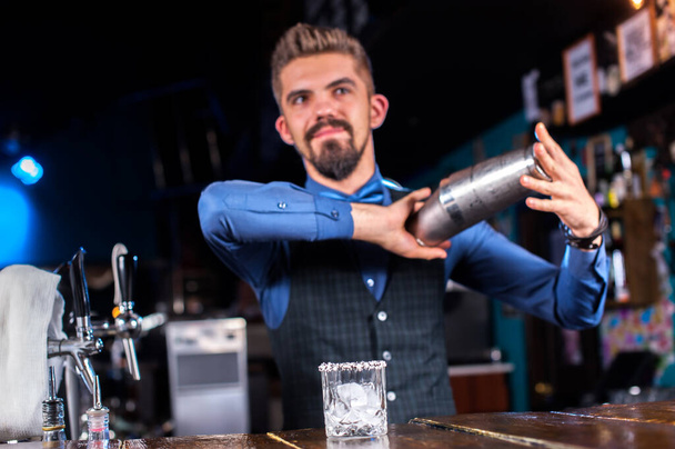 Ο νεαρός μπάρμαν φτιάχνει ένα κοκτέιλ στο μπαρ. - Φωτογραφία, εικόνα