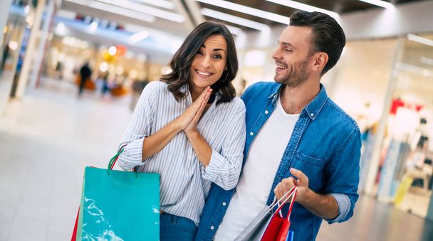 Beautiful happy excited couple in love or family with paper bags in hands while walking during shopping in the mall - Foto, Imagen
