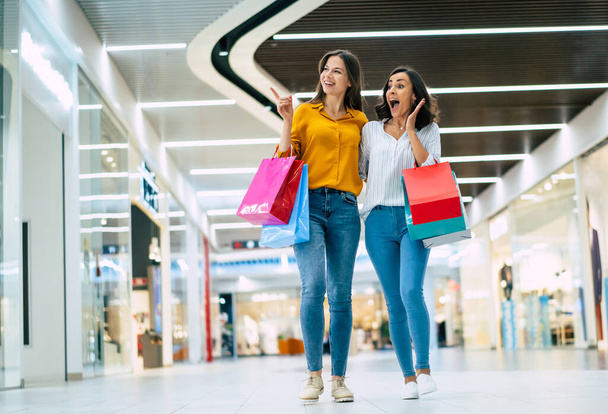 Krásná šťastná a vzrušená mladá dívka přátelé s papírovými taškami jsou procházky po nákupním centru - Fotografie, Obrázek