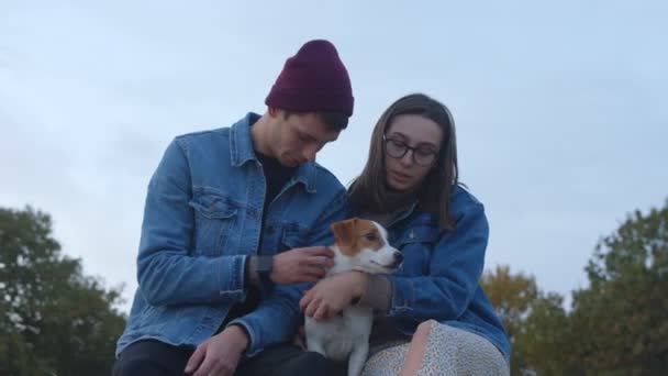 Mladý muž a žena s jack Russell teriér pes sedí na kupce sena ve večerních hodinách - Záběry, video