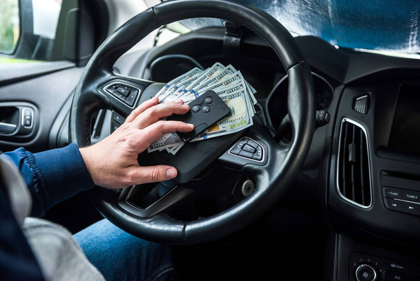 Dollari ja auton avain miehen kädessä auton sisällä. maksaa tavaroita tai vuokrata auton - Valokuva, kuva