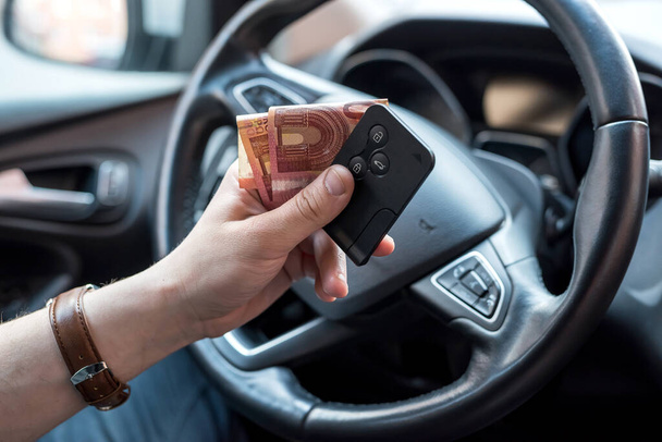 miehen käsi, jolla on euromääräisiä laskuja ja avain auton sisällä ostamista tai vuokraamista varten. rahoitus - Valokuva, kuva