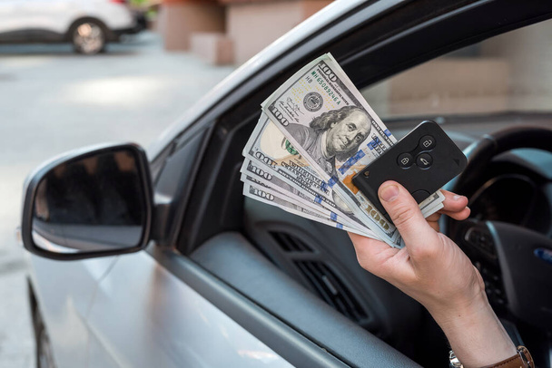 la mano del hombre sentada en el coche sosteniendo el dólar y la llave del coche. concepto de financiación - Foto, imagen