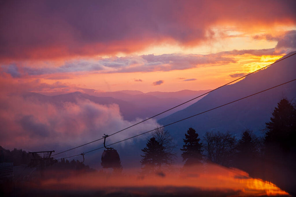 Krasnaya Polyana, Sochi, the mountains of the North Caucasus, snow-capped peaks against the background of autumn trees, red sunset over Krasnaya Polyana by cable car - Photo, Image