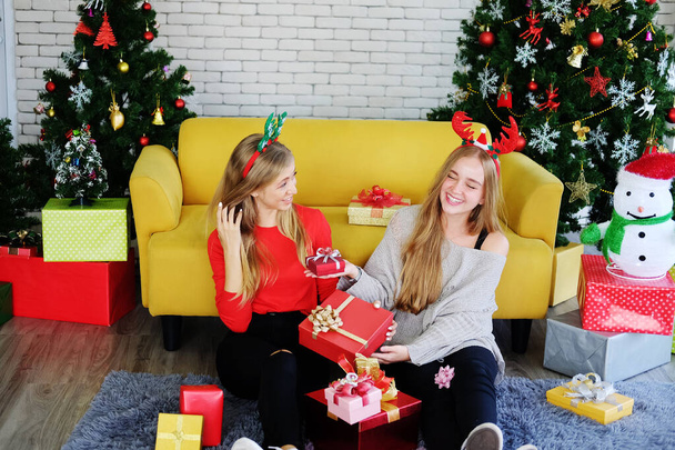 Teenage gülüşü. Kafkasyalı çift yerde oturuyor ve Noel partisinde büyük hediye kutularını tutuyorlar. Tatil konseptinde lezbiyenliğin yaşam tarzı. - Fotoğraf, Görsel