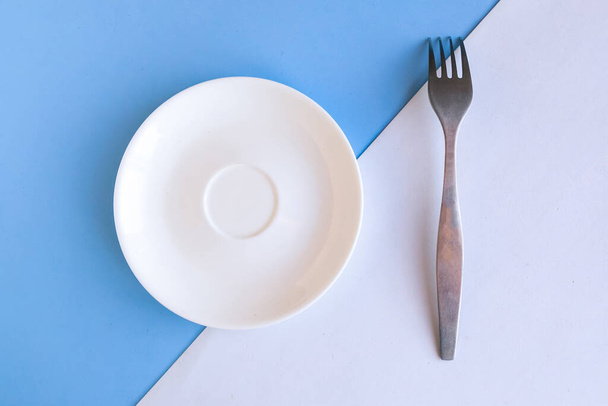 Assiette et fourchette vides sur fond blanc et bleu. Espace de copie pour le texte. Concept minimal - Photo, image
