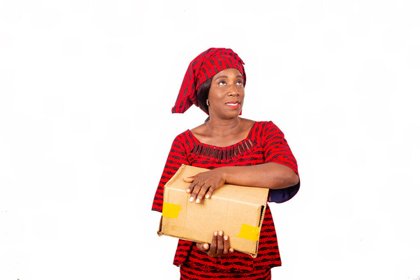 hermosa mujer adulta africana con taparrabo rojo de pie, mirando en el lado sosteniendo una caja de cartón sonriendo aislado sobre un fondo blanco - Foto, imagen