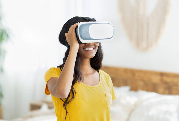 Mujer negra joven con auriculares de realidad virtual explorando el ciberespacio o jugando videojuegos en línea en casa - Foto, imagen