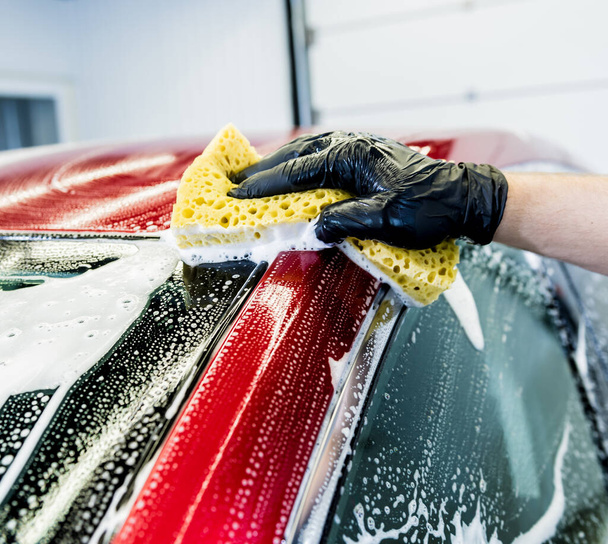 Worker washing red car with sponge on a car wash - Fotó, kép