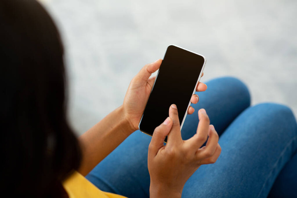 Неузнаваемая черная женщина с помощью мобильного телефона с пустым экраном в помещении, макет для мобильного приложения или дизайна веб-сайта - Фото, изображение