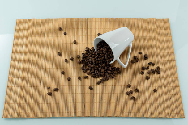 Κύπελλο που βρίσκεται με κόκκους καφέ σε ένα αχυρένιο placemat. - Φωτογραφία, εικόνα