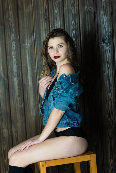 Pretty young girl in black lingerie and jeans jacket sits on bar chair - Фото, зображення