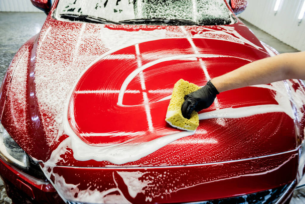 Worker washing red car with sponge on a car wash - Fotoğraf, Görsel