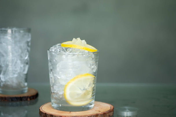 Water glass full of ice cubes with lemon slice on wooden saucer. Summer drink - Foto, afbeelding