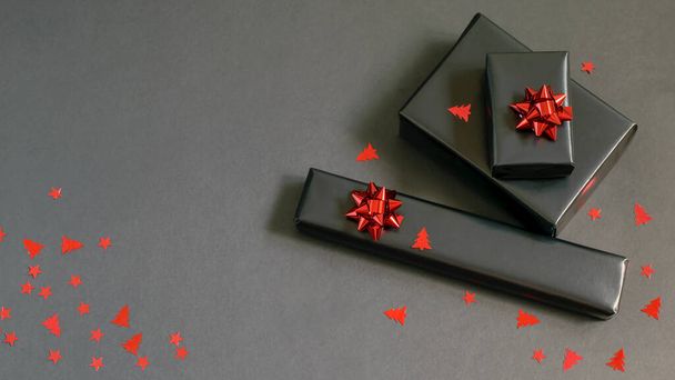 Handmade Christmas gift boxes wrapped in black paper, red sparkle ribbons and festive confetti. Care package, handmade gifts, diy concepts.  - Photo, Image