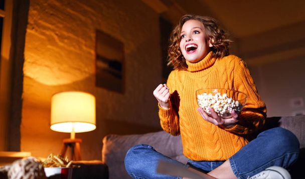 jeune femme gaie enchantée manger pop-corn rit et regarde le film de comédie sur la télévision par câble à la maison en soirée alon - Photo, image