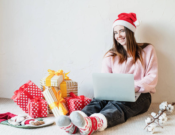 Різдвяне планування, концепція інтернет-магазинів. Молода жінка в Санта-капелюсі покупки в Інтернеті в оточенні подарунків
 - Фото, зображення