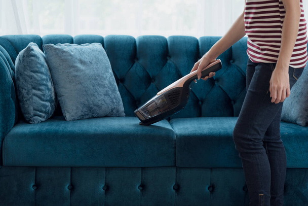 Nahaufnahme einer Hausfrau beim Staubsaugen von Möbeln in einem Haus mit einem tragbaren Handstaubsauger - Foto, Bild