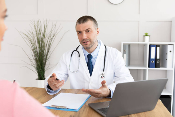 Serious experienced doctor talking to his patient - Foto, imagen