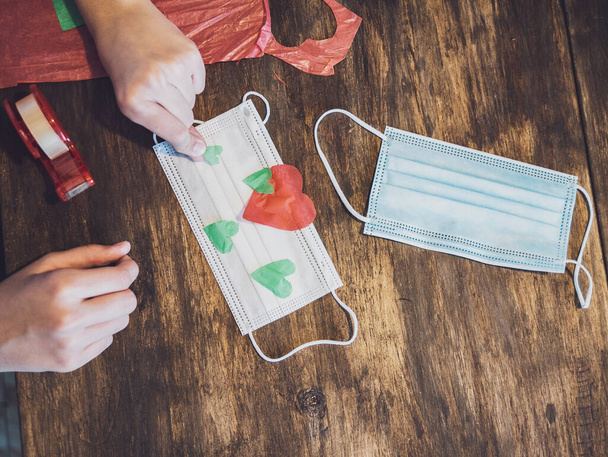Руки молодой девушки, делающей ремесла из бумаги и украшающей хирургическую маску - Фото, изображение
