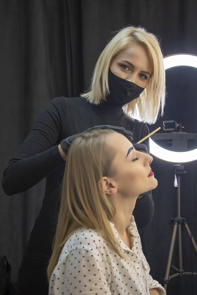 Um mestre maquiador toca as sobrancelhas do cliente com uma escova fina em um salão de beleza. - Foto, Imagem
